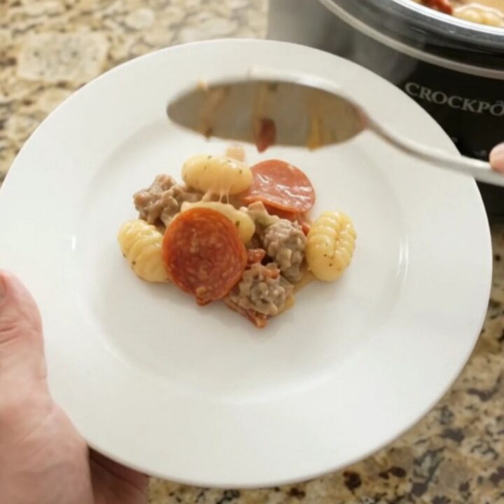 A bubbling Crockpot filled with creamy Boursin pepperoni sausage gnocchi, topped with melted fontina and steam rising.