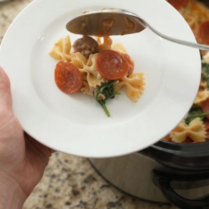 Slow cooker filled with bubbling pepperoni sausage pesto farfalle