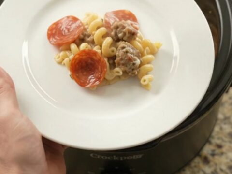 Crockpot full of creamy cavatappi with pepperoni and sausage, topped with melted provolone