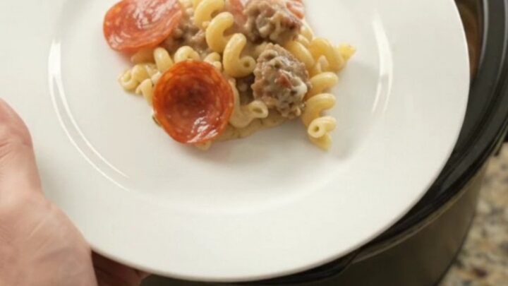 Crockpot full of creamy cavatappi with pepperoni and sausage, topped with melted provolone