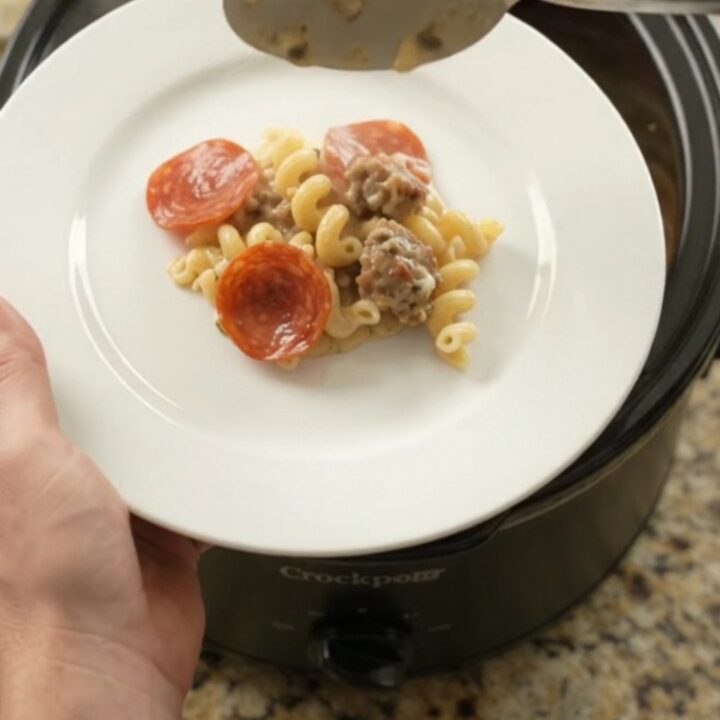 Crockpot full of creamy cavatappi with pepperoni and sausage, topped with melted provolone