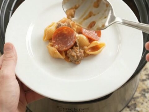 Slow cooker filled with creamy pasta, pepperoni, and sausage, topped with melted provolone