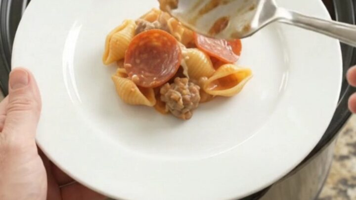 Slow cooker filled with creamy pasta, pepperoni, and sausage, topped with melted provolone
