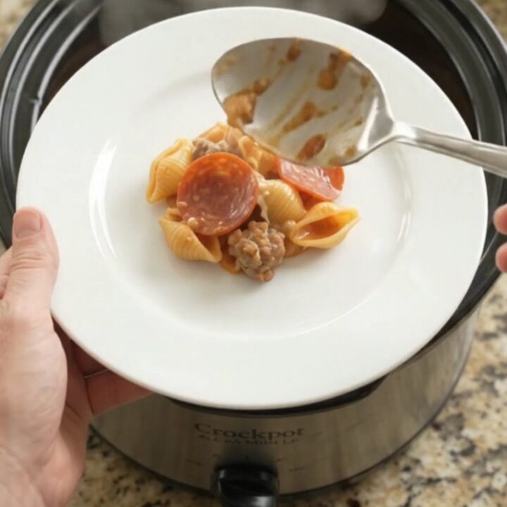 Slow cooker filled with creamy pasta, pepperoni, and sausage, topped with melted provolone