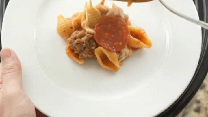 A bubbling slow cooker filled with creamy pasta, pepperoni, and sausage, topped with melted cheese.