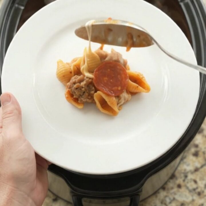 A bubbling slow cooker filled with creamy pasta, pepperoni, and sausage, topped with melted cheese.