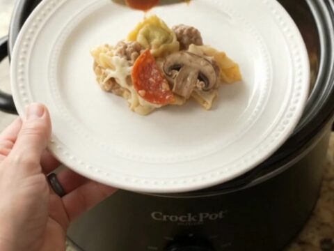 Slow cooker pepperoni tortellini Alfredo with melted cheese and sausage in a black Crockpot