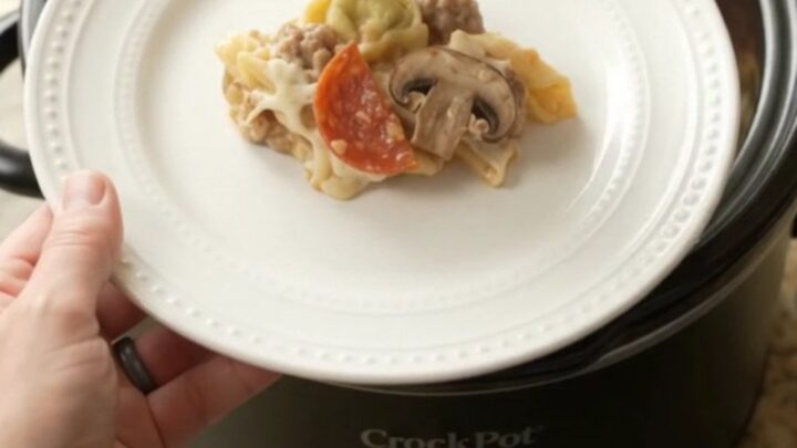 Slow cooker pepperoni tortellini Alfredo with melted cheese and sausage in a black Crockpot