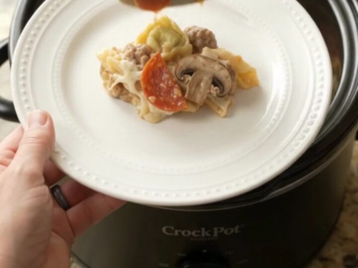 Slow cooker pepperoni tortellini Alfredo with melted cheese and sausage in a black Crockpot