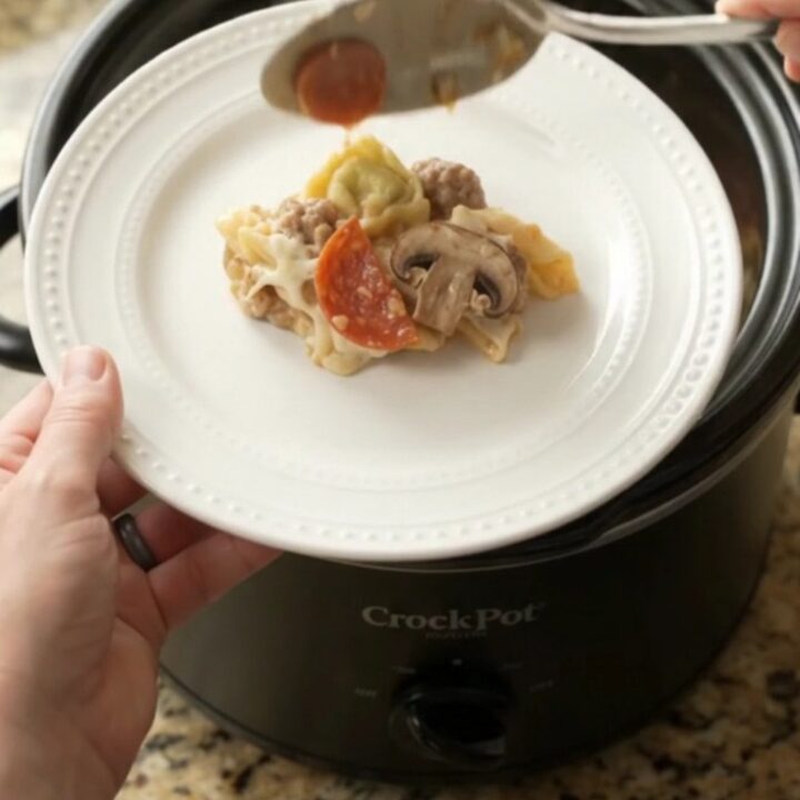 Slow cooker pepperoni tortellini Alfredo with melted cheese and sausage in a black Crockpot