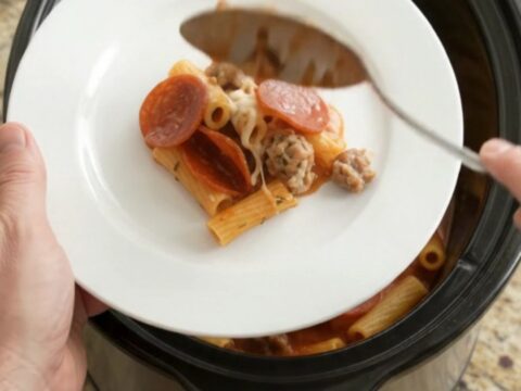 Slow cooker baked ziti with pepperoni, sausage, and melted cheese in a black crockpot