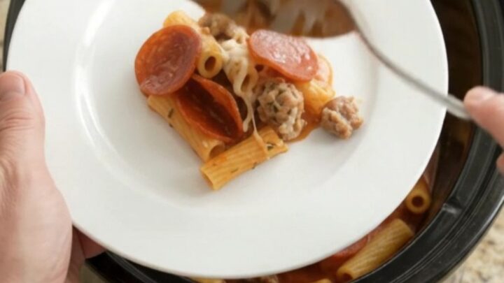 Slow cooker baked ziti with pepperoni, sausage, and melted cheese in a black crockpot