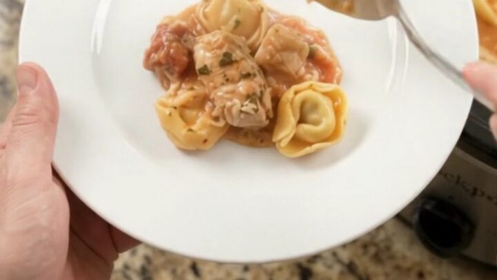 Crockpot chicken tortellini marinara with melted mozzarella and cream cheese sauce, served in a black slow cooker.