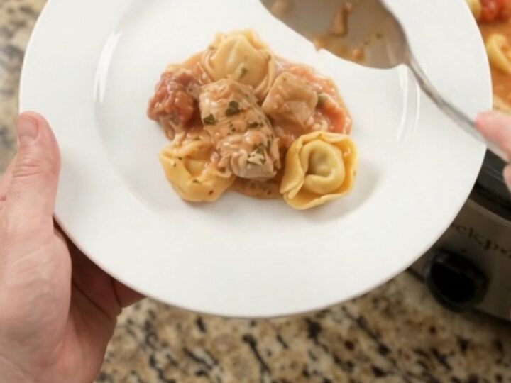 Crockpot chicken tortellini marinara with melted mozzarella and cream cheese sauce, served in a black slow cooker.