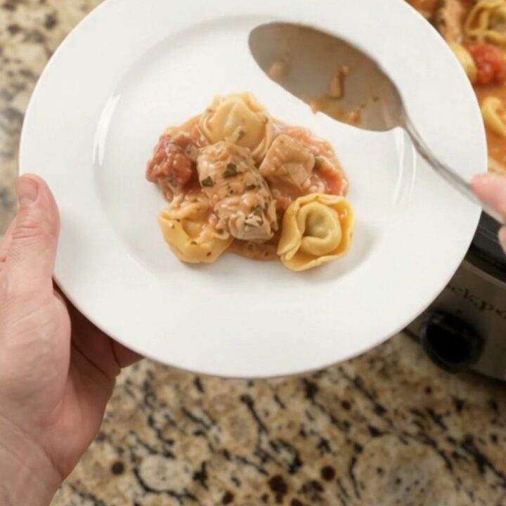 Crockpot chicken tortellini marinara with melted mozzarella and cream cheese sauce, served in a black slow cooker.