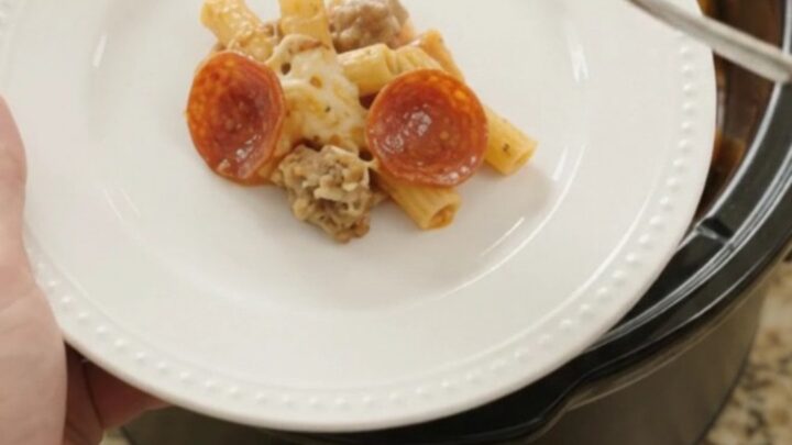 Bubbling slow cooker ziti with pepperoni, sausage, and melted cheese, served in a black Crockpot.