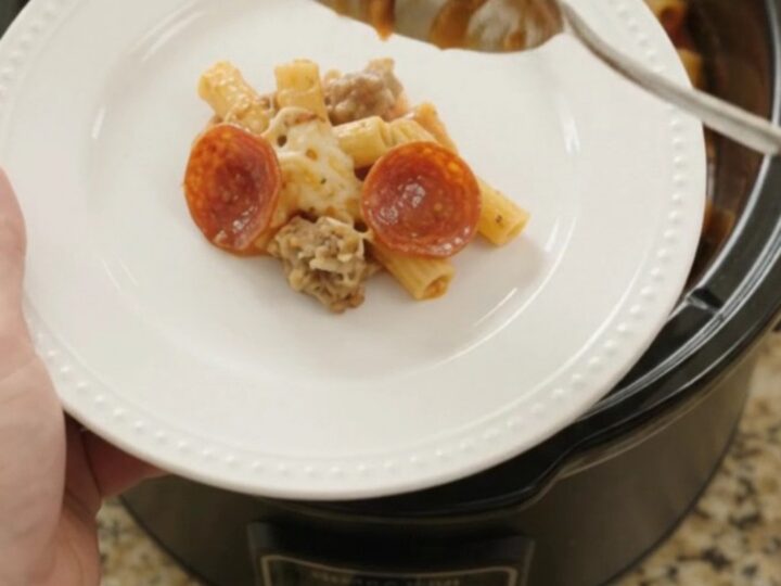Bubbling slow cooker ziti with pepperoni, sausage, and melted cheese, served in a black Crockpot.