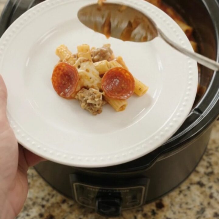 Bubbling slow cooker ziti with pepperoni, sausage, and melted cheese, served in a black Crockpot.