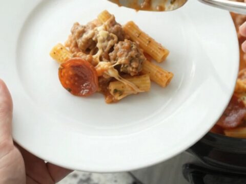 Slow cooker filled with bubbling baked ziti topped with melted provolone and ricotta
