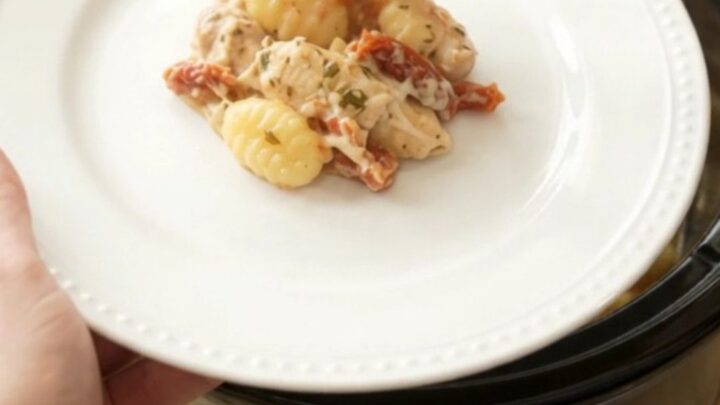 A creamy Crockpot chicken Tuscan gnocchi in a black slow cooker, with melted mozzarella and sun-dried tomatoes.