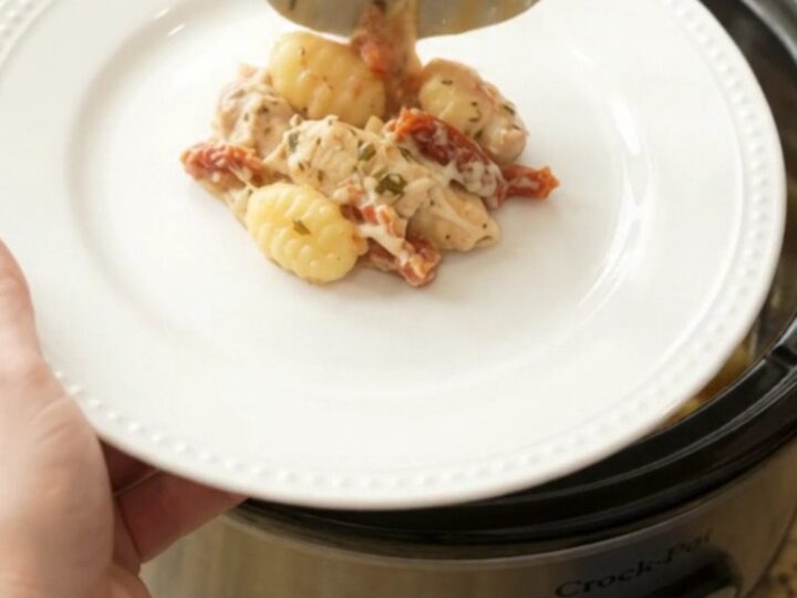 A creamy Crockpot chicken Tuscan gnocchi in a black slow cooker, with melted mozzarella and sun-dried tomatoes.