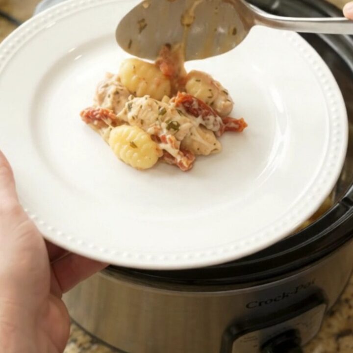 A creamy Crockpot chicken Tuscan gnocchi in a black slow cooker, with melted mozzarella and sun-dried tomatoes.