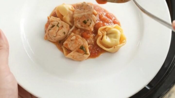 Slow cooker filled with chicken tortellini in marinara sauce, topped with melted Italian cheeses and Parmesan