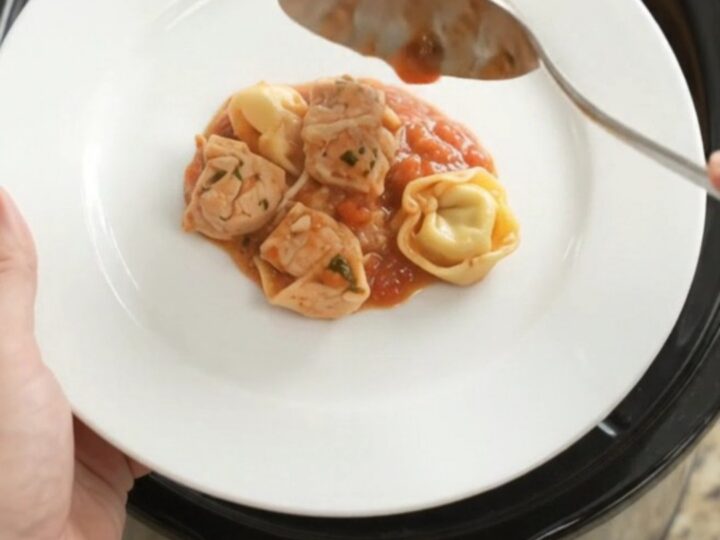 Slow cooker filled with chicken tortellini in marinara sauce, topped with melted Italian cheeses and Parmesan