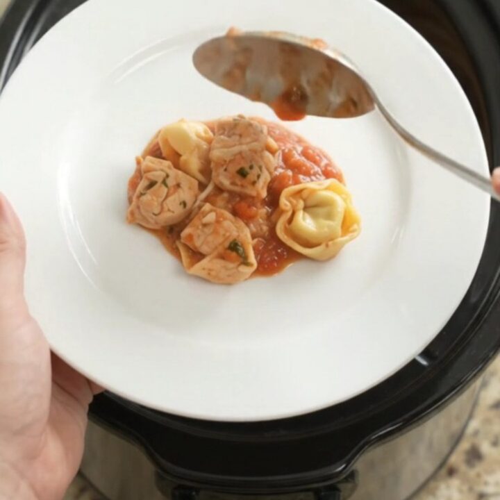 Slow cooker filled with chicken tortellini in marinara sauce, topped with melted Italian cheeses and Parmesan