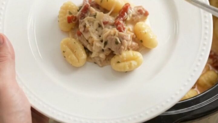 Slow cooker filled with creamy chicken gnocchi topped with melted cheese and sun-dried tomatoes