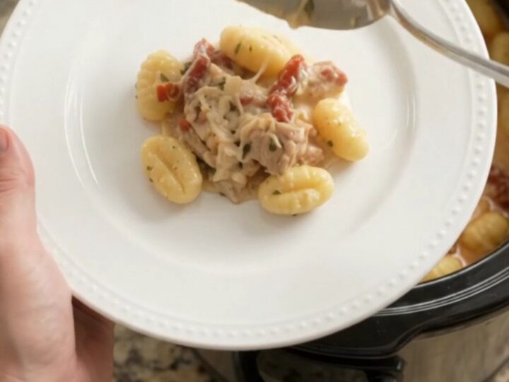 Slow cooker filled with creamy chicken gnocchi topped with melted cheese and sun-dried tomatoes