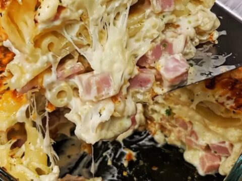 A towering, decadent slice of creamy ham and cheese lasagna held mid-air, showing melted cheese and ham pockets.