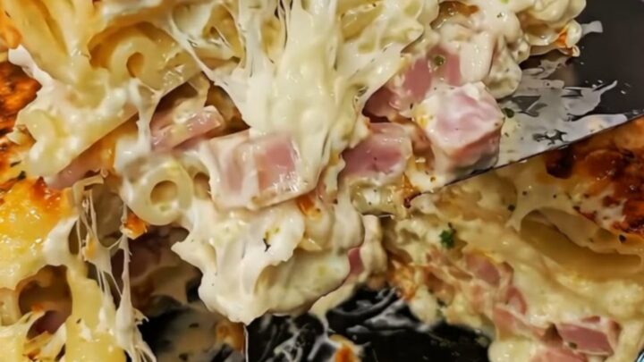 A towering, decadent slice of creamy ham and cheese lasagna held mid-air, showing melted cheese and ham pockets.