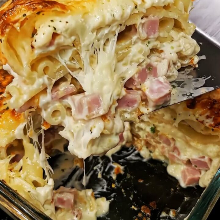 A towering, decadent slice of creamy ham and cheese lasagna held mid-air, showing melted cheese and ham pockets.