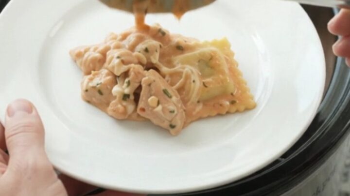 Slow cooker chicken vodka ravioli in a black Crockpot, topped with melted mozzarella and creamy pink sauce.