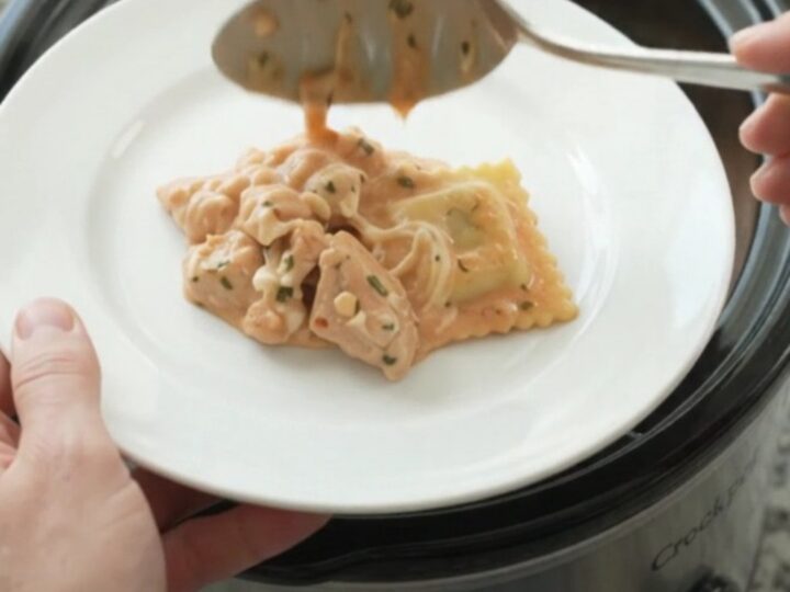 Slow cooker chicken vodka ravioli in a black Crockpot, topped with melted mozzarella and creamy pink sauce.