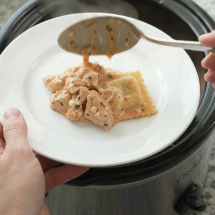 Slow cooker chicken vodka ravioli in a black Crockpot, topped with melted mozzarella and creamy pink sauce.