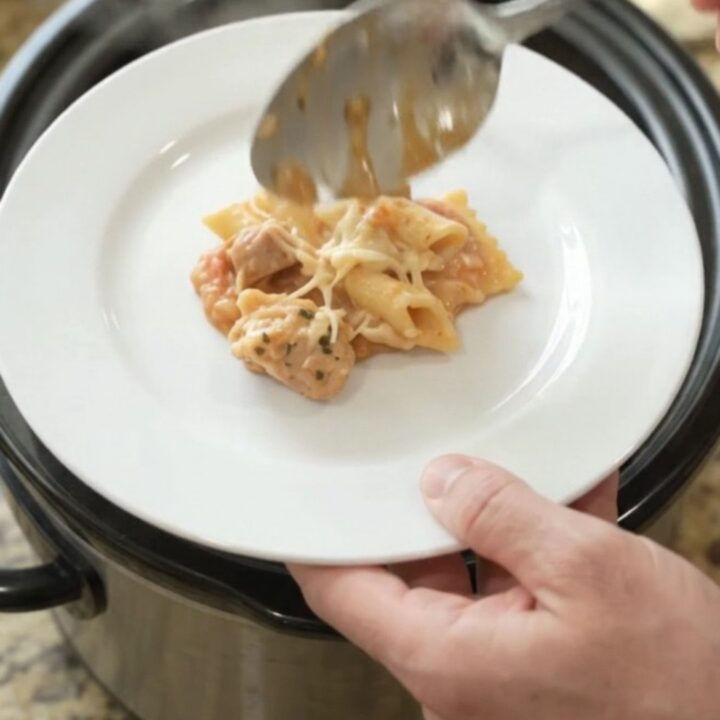Slow cooker filled with cheesy chicken vodka ravioli, topped with melted Italian cheeses and Parmesan.