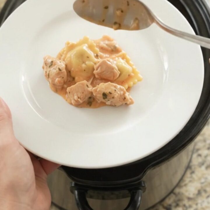 Crockpot Boursin Chicken Vodka Ravioli in a black slow cooker with melted cheese and sauce.