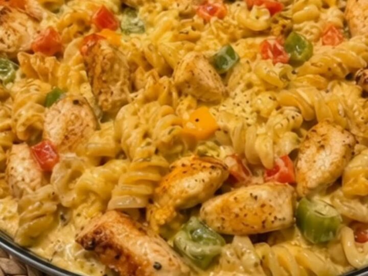 A close-up shot of a large skillet filled with creamy Rotel chicken pasta, garnished with peppers and seared chicken pieces.
