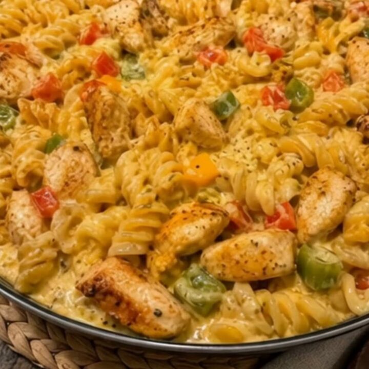A close-up shot of a large skillet filled with creamy Rotel chicken pasta, garnished with peppers and seared chicken pieces.