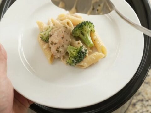 Slow cooker filled with creamy chicken Alfredo penne and broccoli, topped with melted mozzarella.