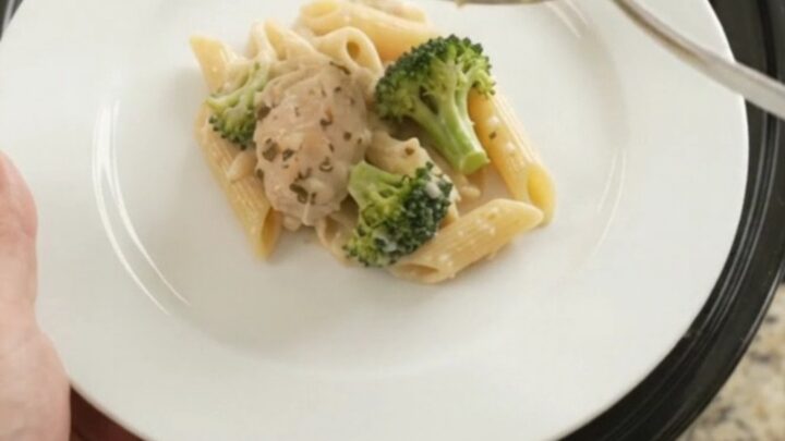 Slow cooker filled with creamy chicken Alfredo penne and broccoli, topped with melted mozzarella.