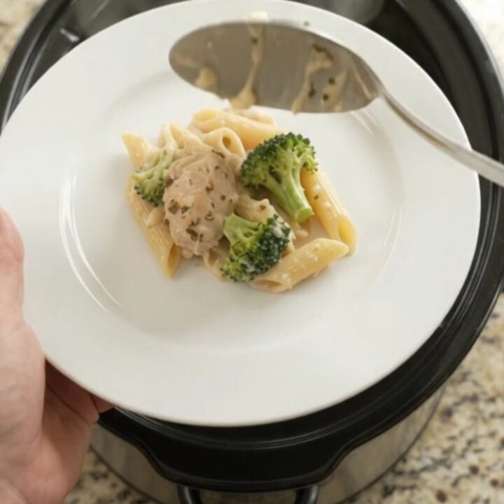 Slow cooker filled with creamy chicken Alfredo penne and broccoli, topped with melted mozzarella.