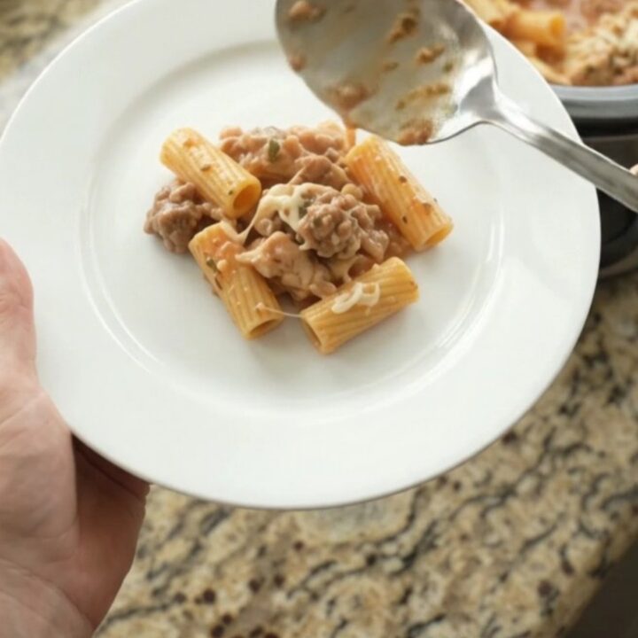 Creamy Boursin chicken rigatoni in a black slow cooker, topped with melted fontina and fresh herbs.