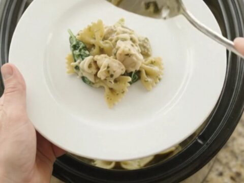 Bubbling slow cooker full of creamy chicken pesto farfalle with melted mozzarella