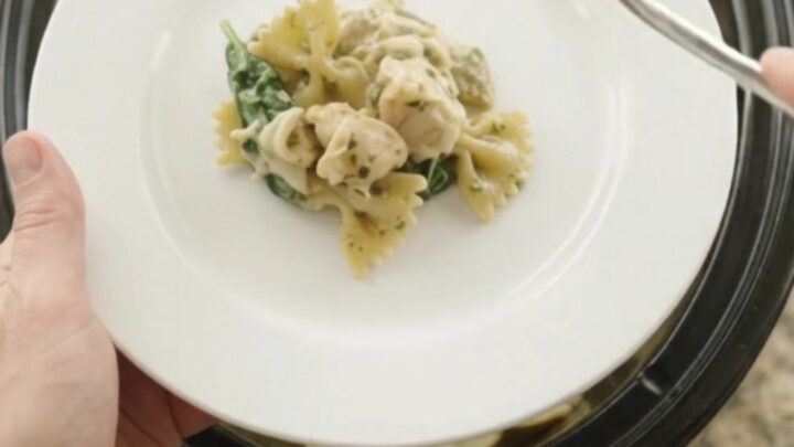 Bubbling slow cooker full of creamy chicken pesto farfalle with melted mozzarella