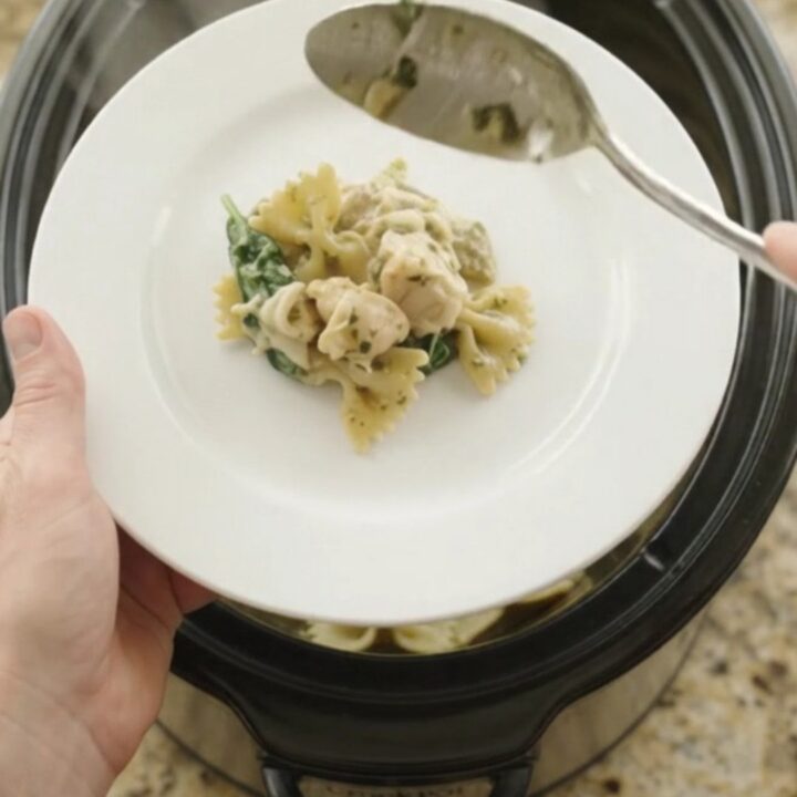 Bubbling slow cooker full of creamy chicken pesto farfalle with melted mozzarella
