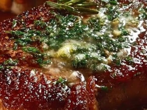 A thick, perfectly seared steak topped with melting garlic herb butter on a rustic wooden board.