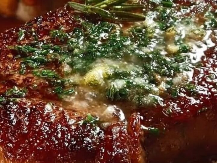 A thick, perfectly seared steak topped with melting garlic herb butter on a rustic wooden board.